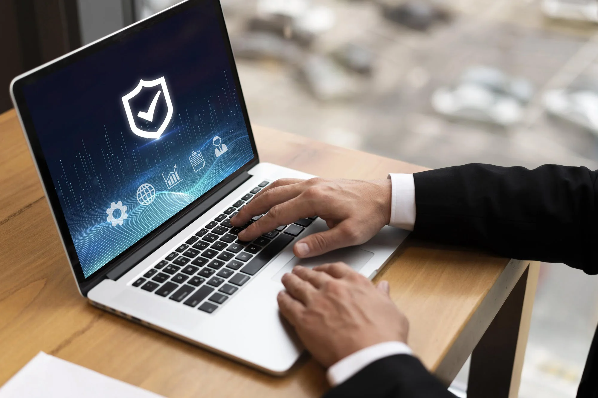 A person in a suit uses a laptop showing a security shield icon on the screen. The office setting and digital symbols suggest cybersecurity themes